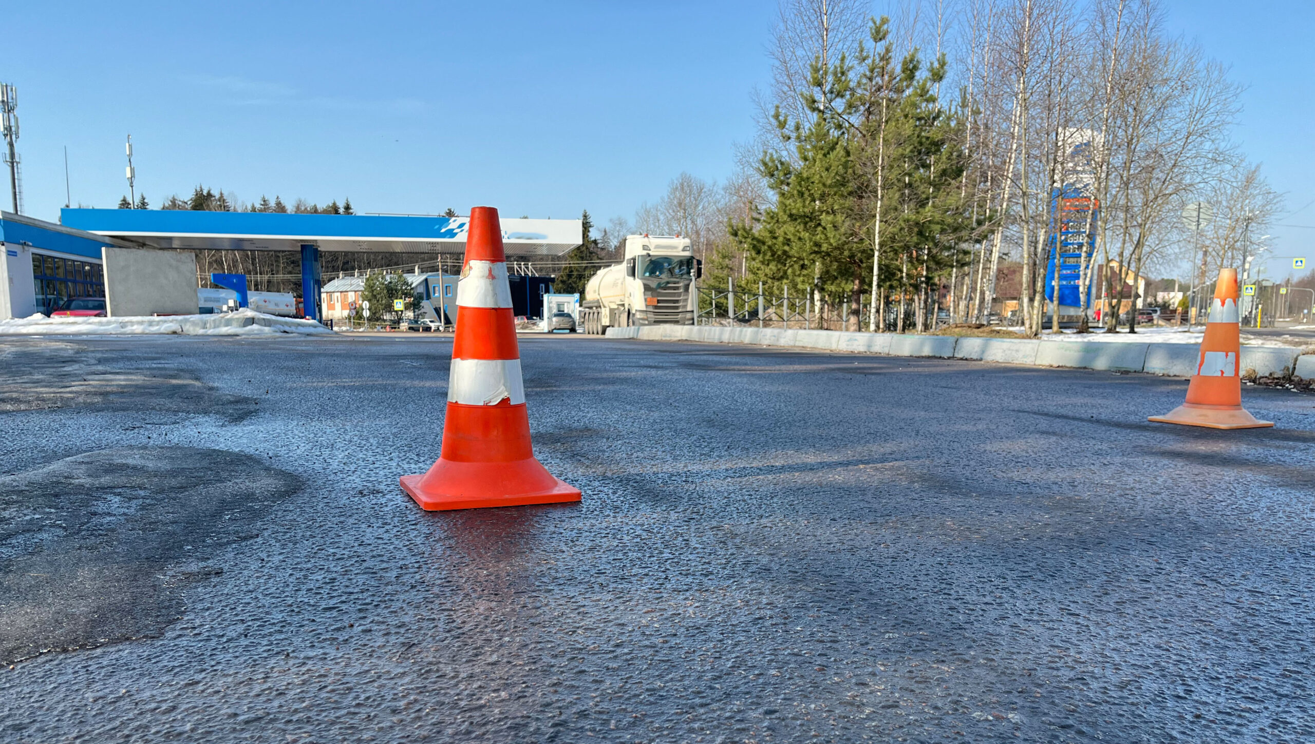 Traffic cones placed on a wet asphalt surface near a gas station on a sunny day Water Problems